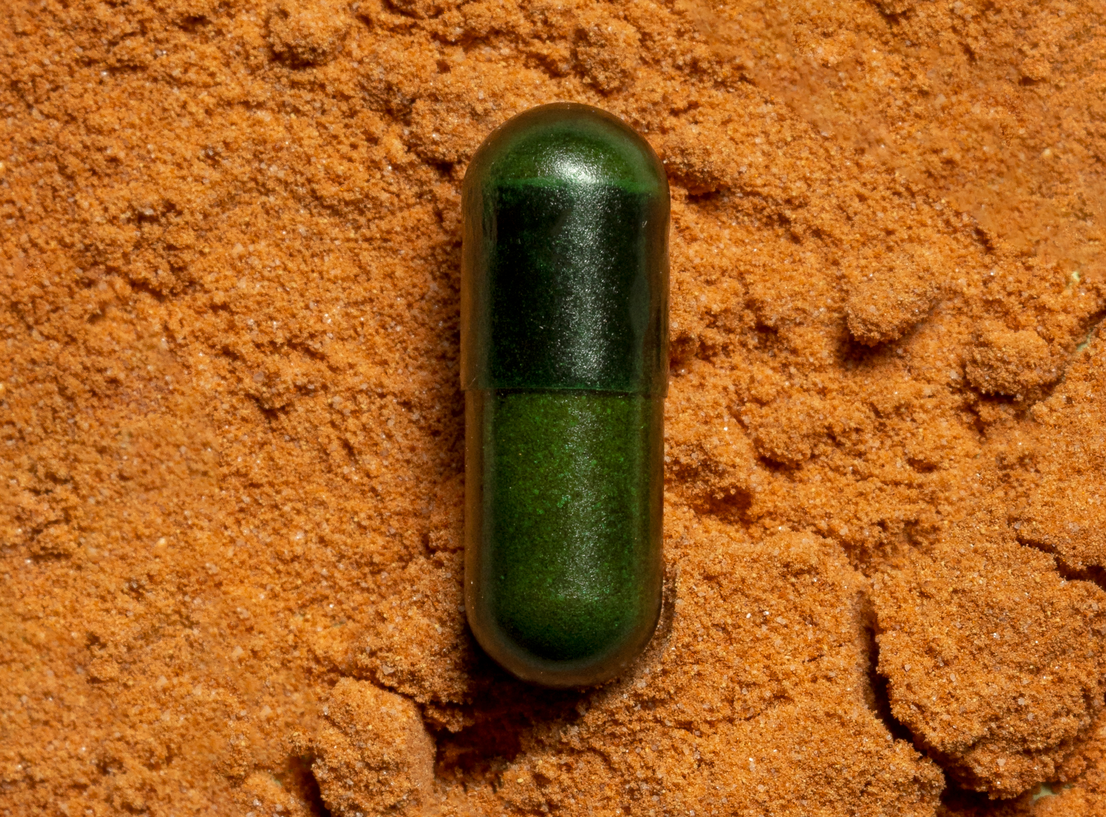 Nahaufnahme einer grünen tigovit EGCG Kapsel auf feinem, braunem Grüntee-Extrakt Pulver.