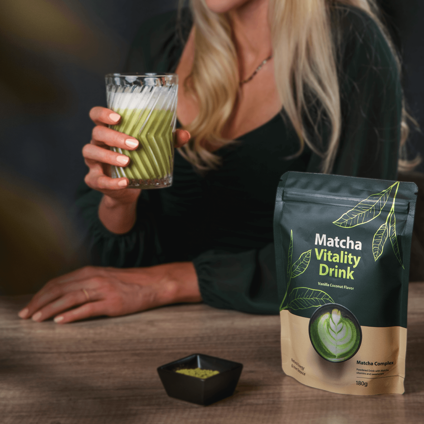 Frau genießt cremigen Bio Matcha Kollagen Drink Vanille-Kokos neben 180g Packung Matcha Vitality Drink.